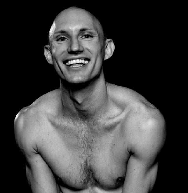black and white image of a barechested person with a bald head and a wide smile
