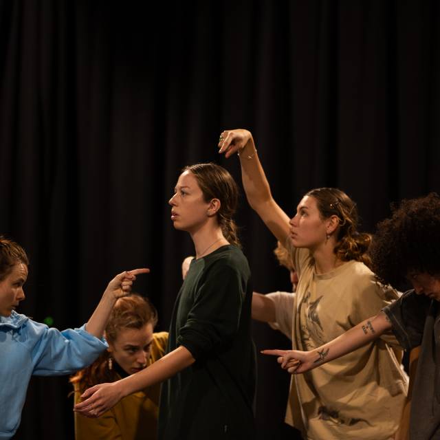 Group of 6 dancers with one finger pointed at one dancer in the center of the group