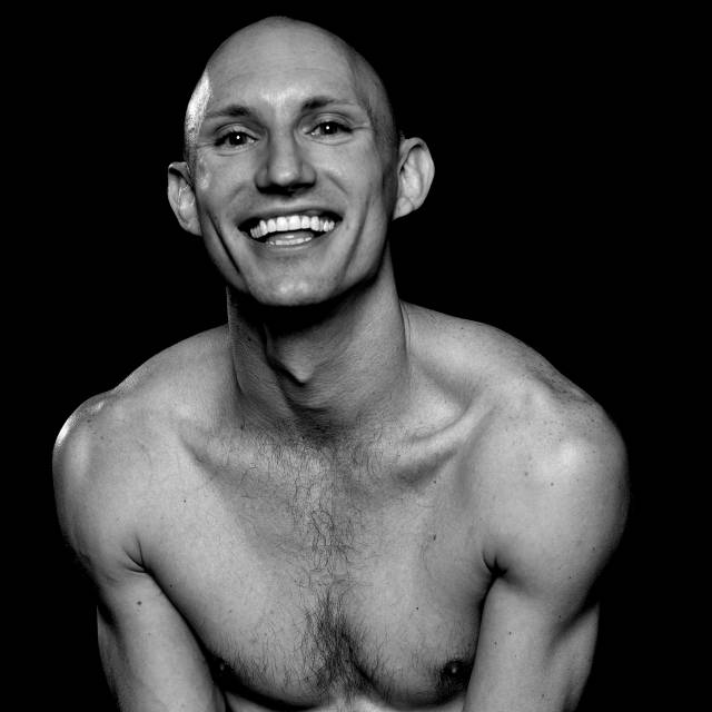 black and white image of a barechested person with a bald head and a wide smile